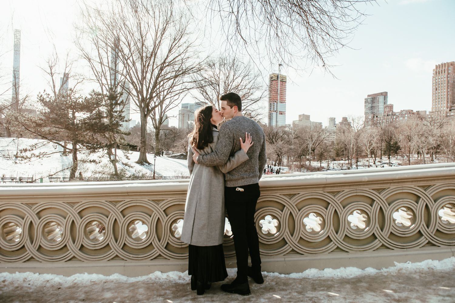 Couple sharing intimate moment by decorative stone railing in winter park setting.