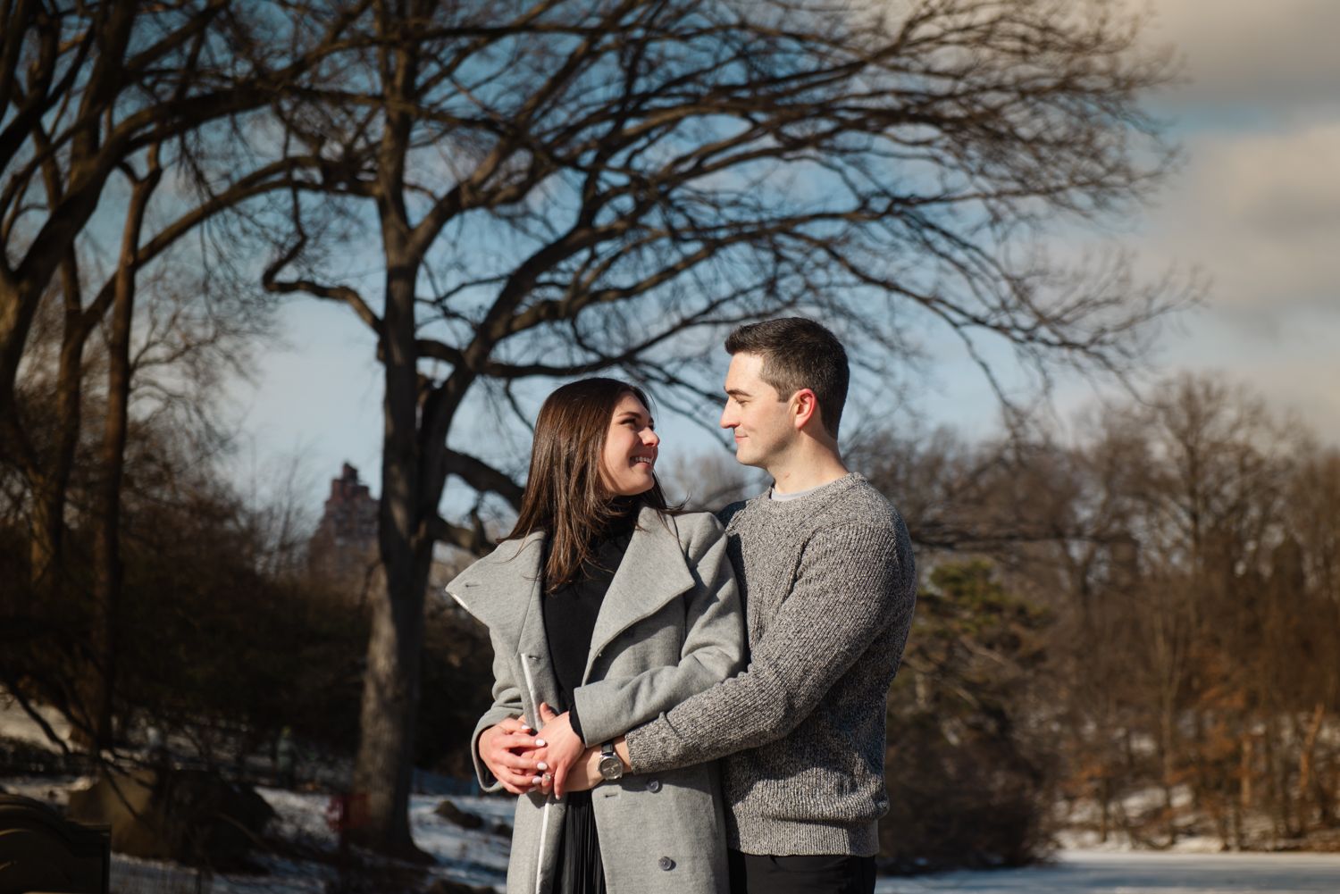 Romantic winter engagement photos with couple in grey sweaters against snowy landscape.