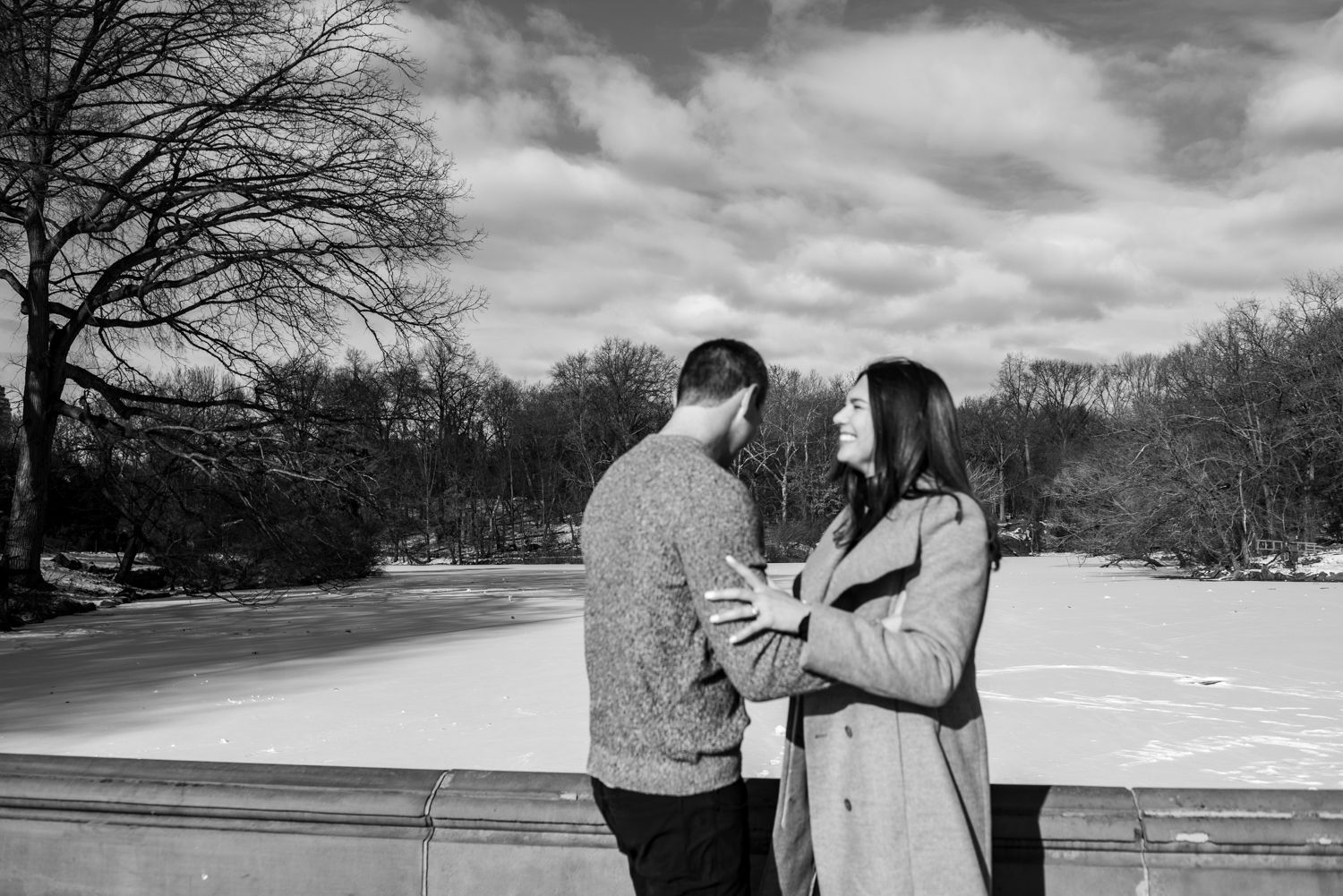 Black and white winter landscape with couple by stone railing and bare trees.