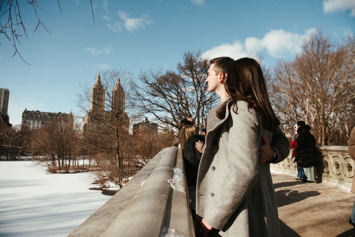 Winter engagement photoshoot in a snow-covered park with decorative stone railings.