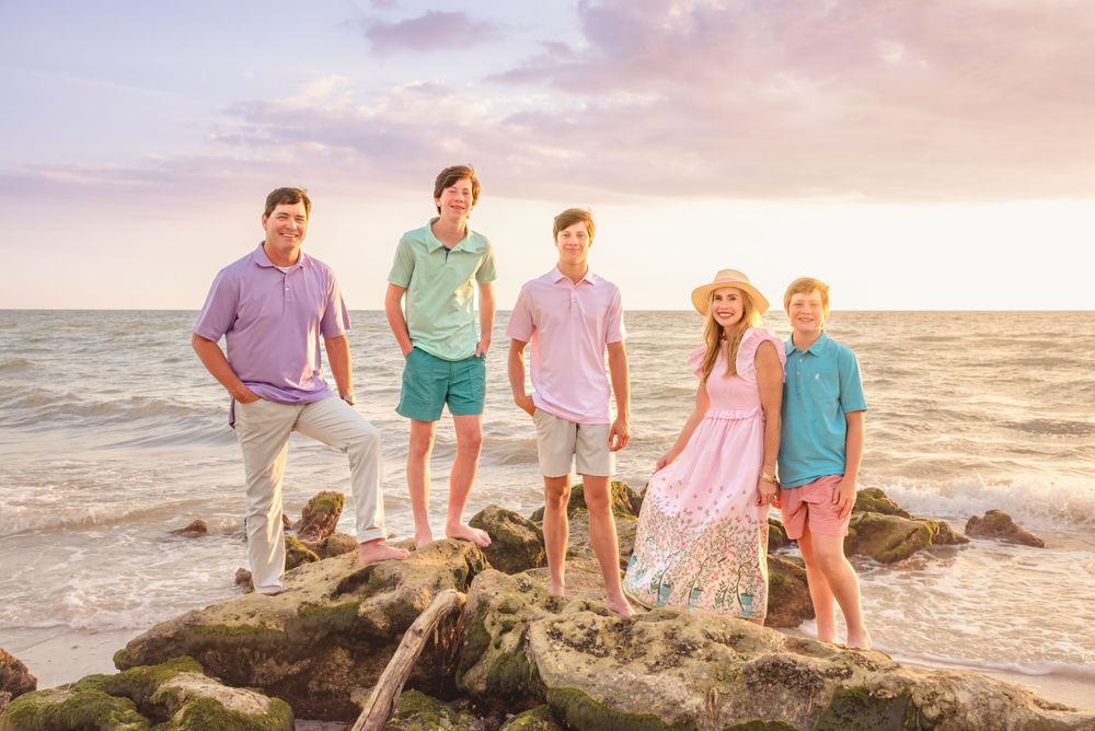 family portrait standing on rocks at Florida beach with sunset