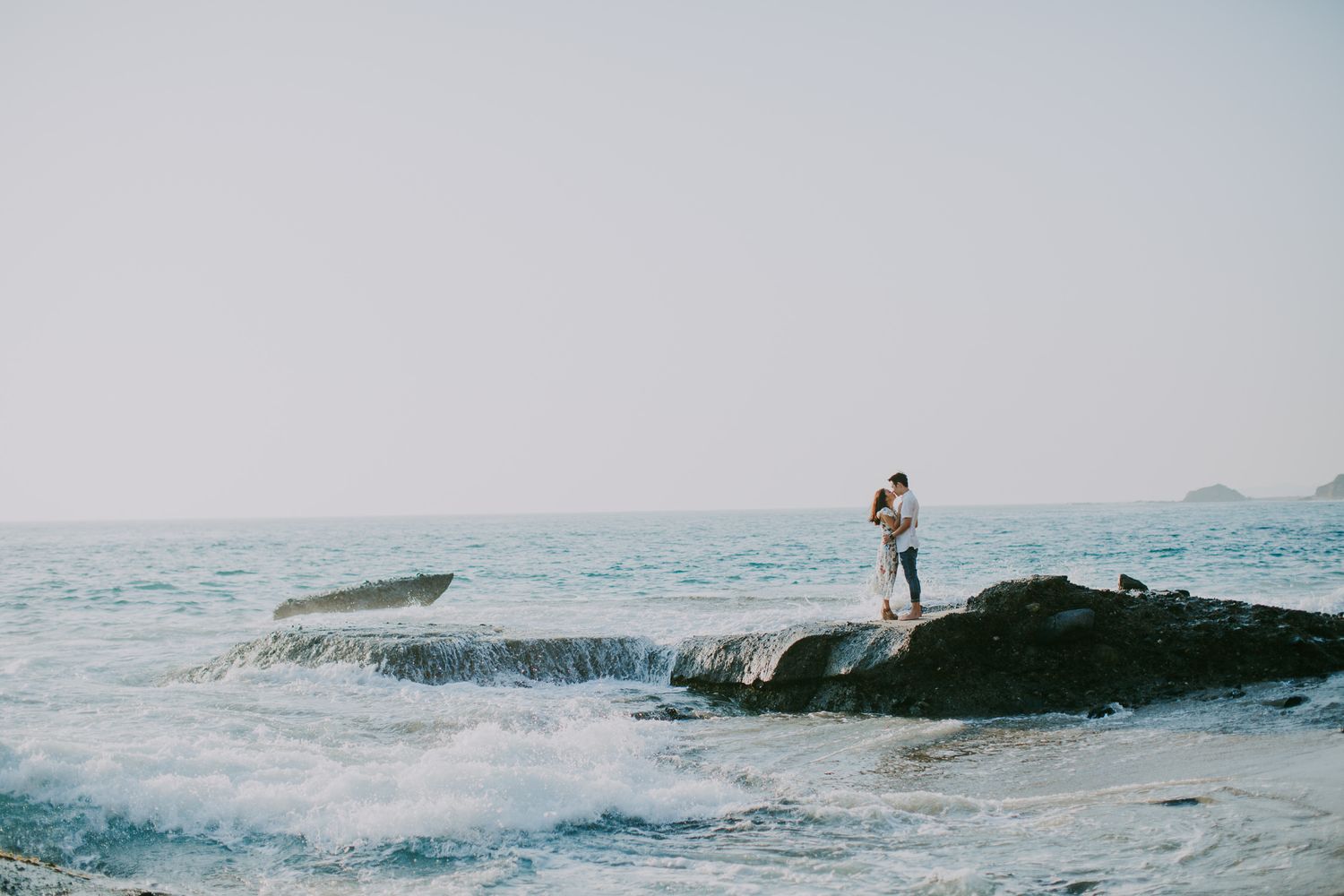 Silhouetted figure standing on rocky outcrop overlooking ocean waves.