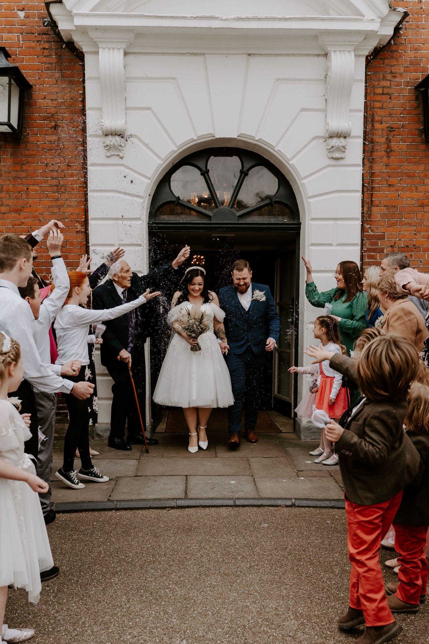 bride and groom laughing as guests throw purple confetti over them.