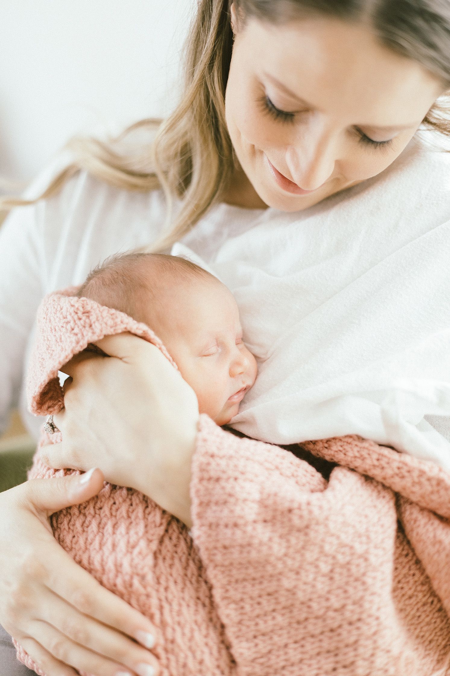 Intimate portrait of sleeping newborn wrapped in pink knit blanket resting against caregiver.