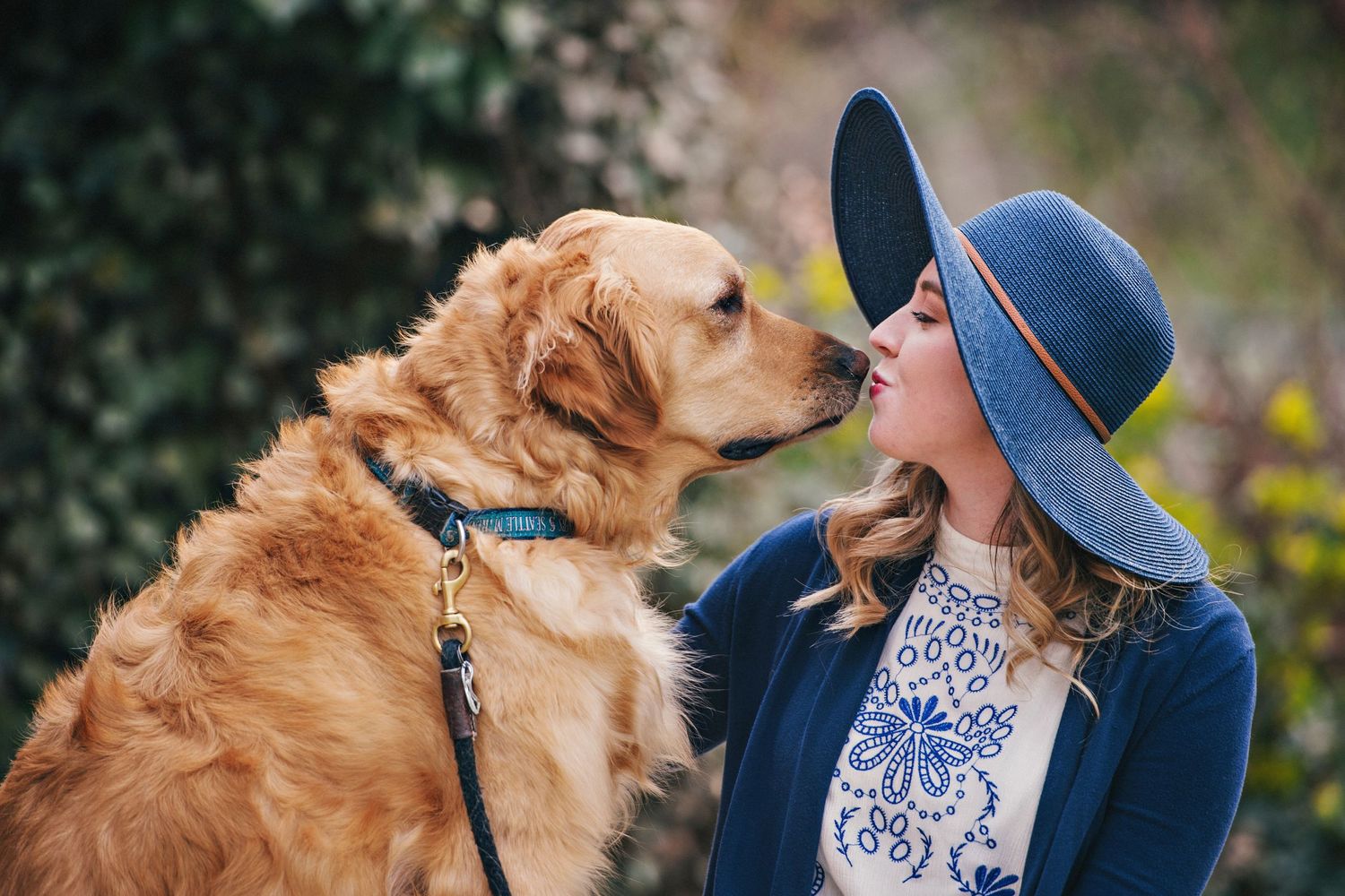 A handsome golden retriever gets a kiss from his lady wearing a hat