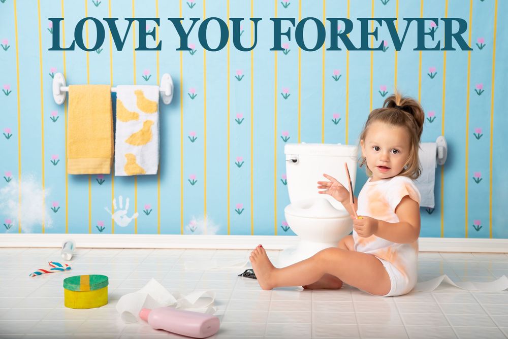 Baby sitting against blue wallpaper with 'Love You Forever' text and nursery decorations.