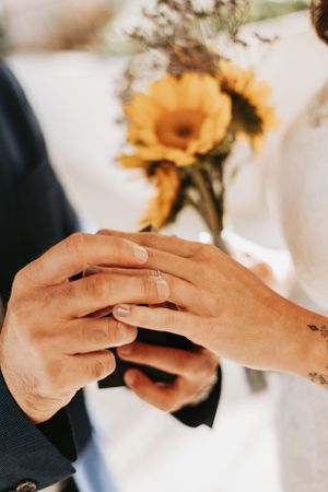 Close-up of hands exchanging rings with sunflowers in the background.