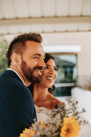 A joyful couple poses with sunflowers during their wedding celebration.