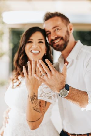 Two hands showing off engagement rings with one featuring intricate henna tattoo designs.