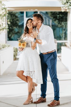 A romantic moment captured outdoors with a couple wearing white and holding a bouquet.