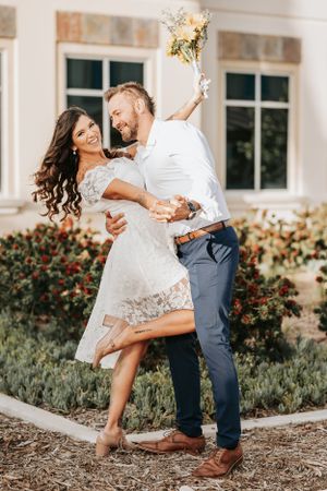 A romantic dancing pose outdoors with sunflowers against a building backdrop.