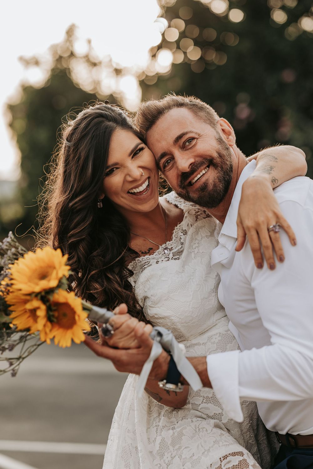 Happy couple embraces while holding sunflowers during their wedding photoshoot.