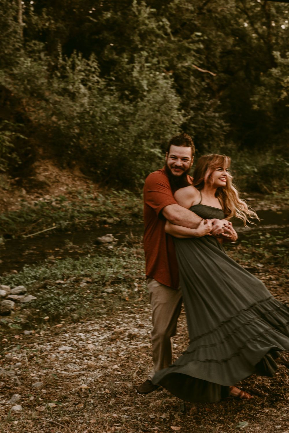 Playful couple dancing together on a forest path in autumn tones.