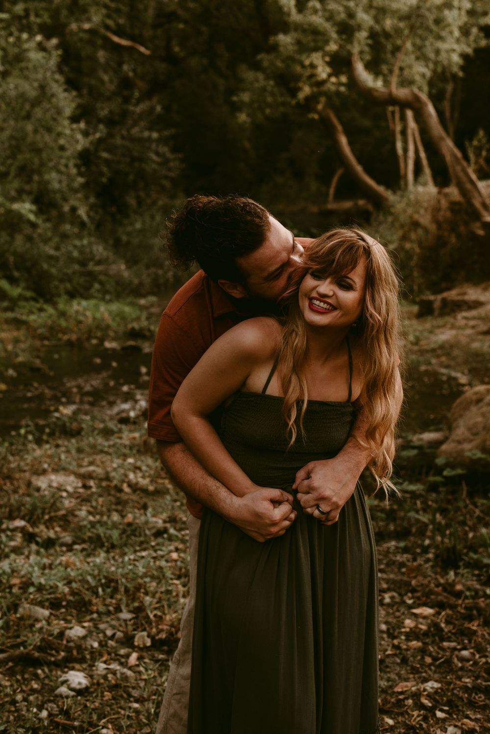 Joyful couple sharing a laugh while embracing in a forest setting.