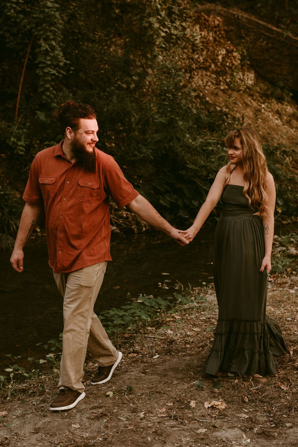Couple holding hands while walking through a wooded trail in coordinated outfits.