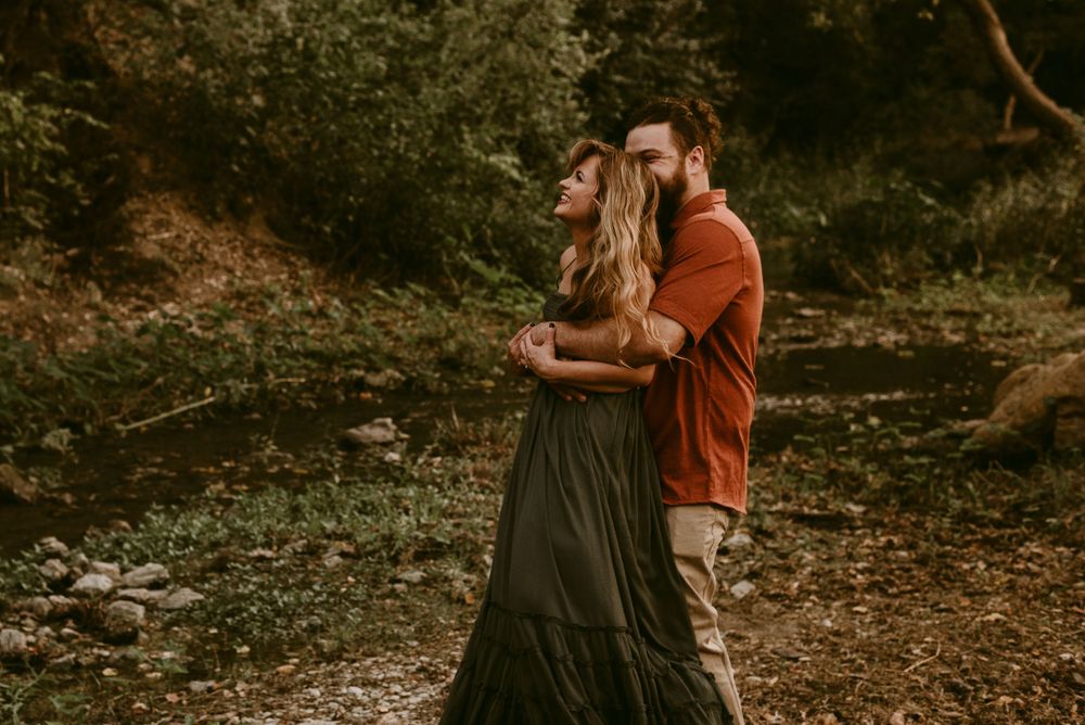 Couple in rust and dark clothing sharing an intimate dance in the woods.