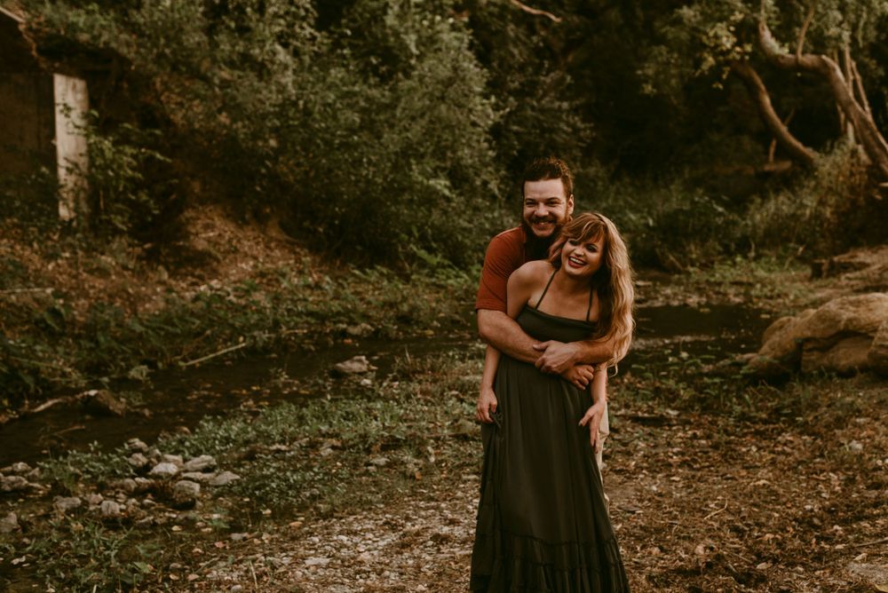 Couple in coordinated outfits embracing in a natural woodland setting.