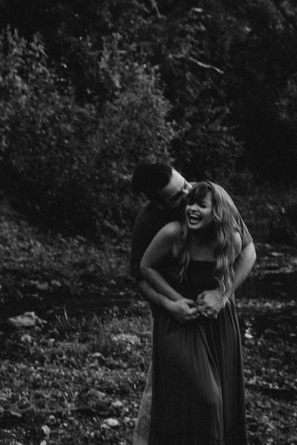 Black and white candid moment of couple laughing together outdoors.