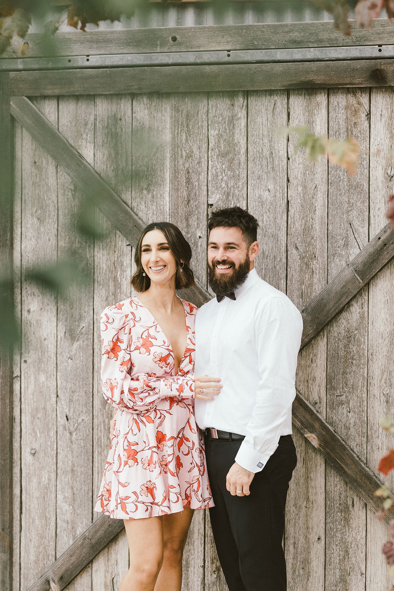 Couple posing against rustic wooden fence outdoors.