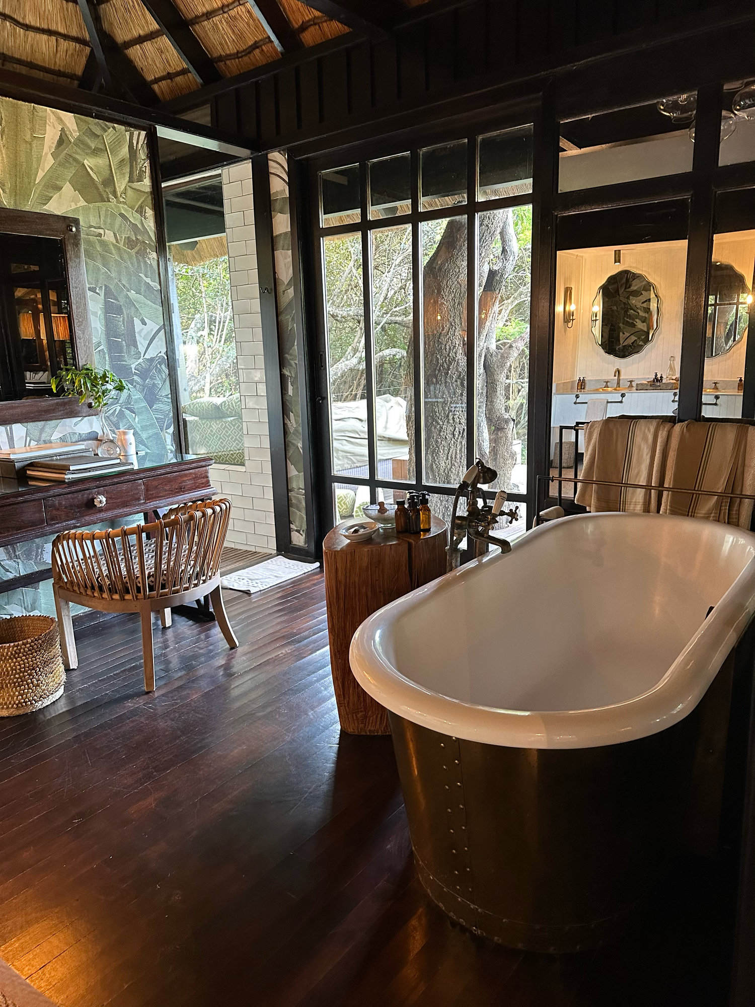 A luxury bathroom with freestanding tub and wooden floors, featuring large windows with views of the outdoors.