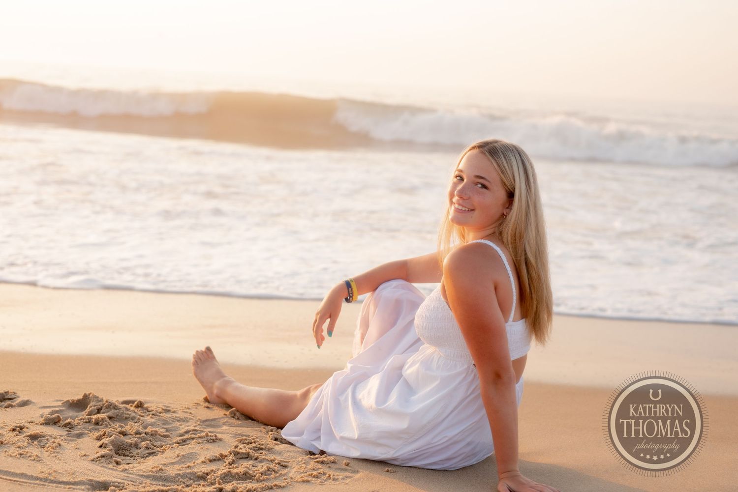 Someone relaxes on sandy beach in white dress during golden hour.
