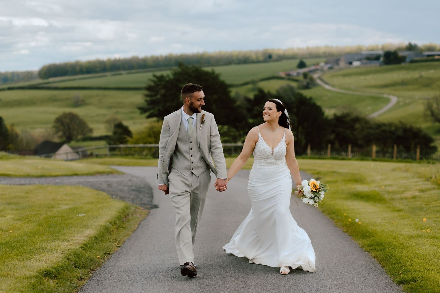 A couple walks hand in hand along a scenic countryside path surrounded by rolling green hills.