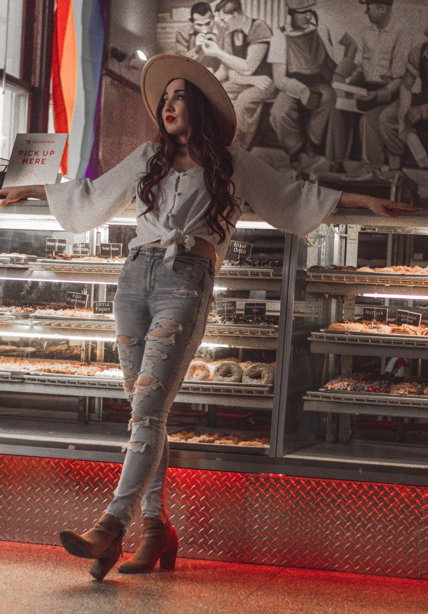 Woman in vintage hat and ripped jeans posing at retro-style bakery counter.