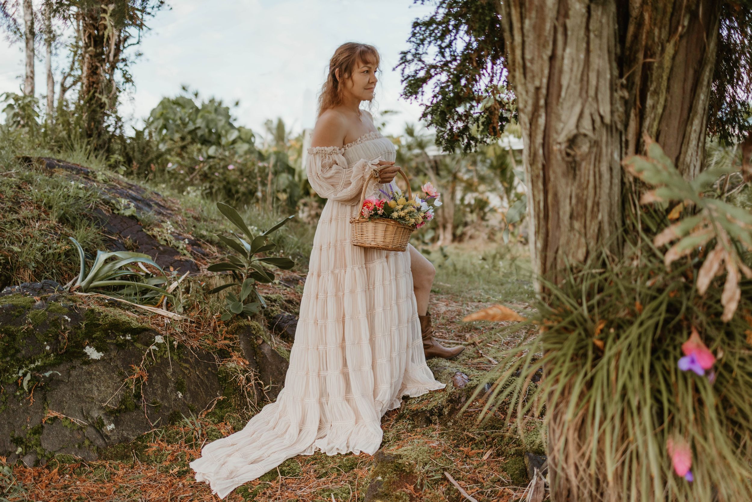 Someone in a flowing white wedding dress holds a bouquet in a tropical garden setting.