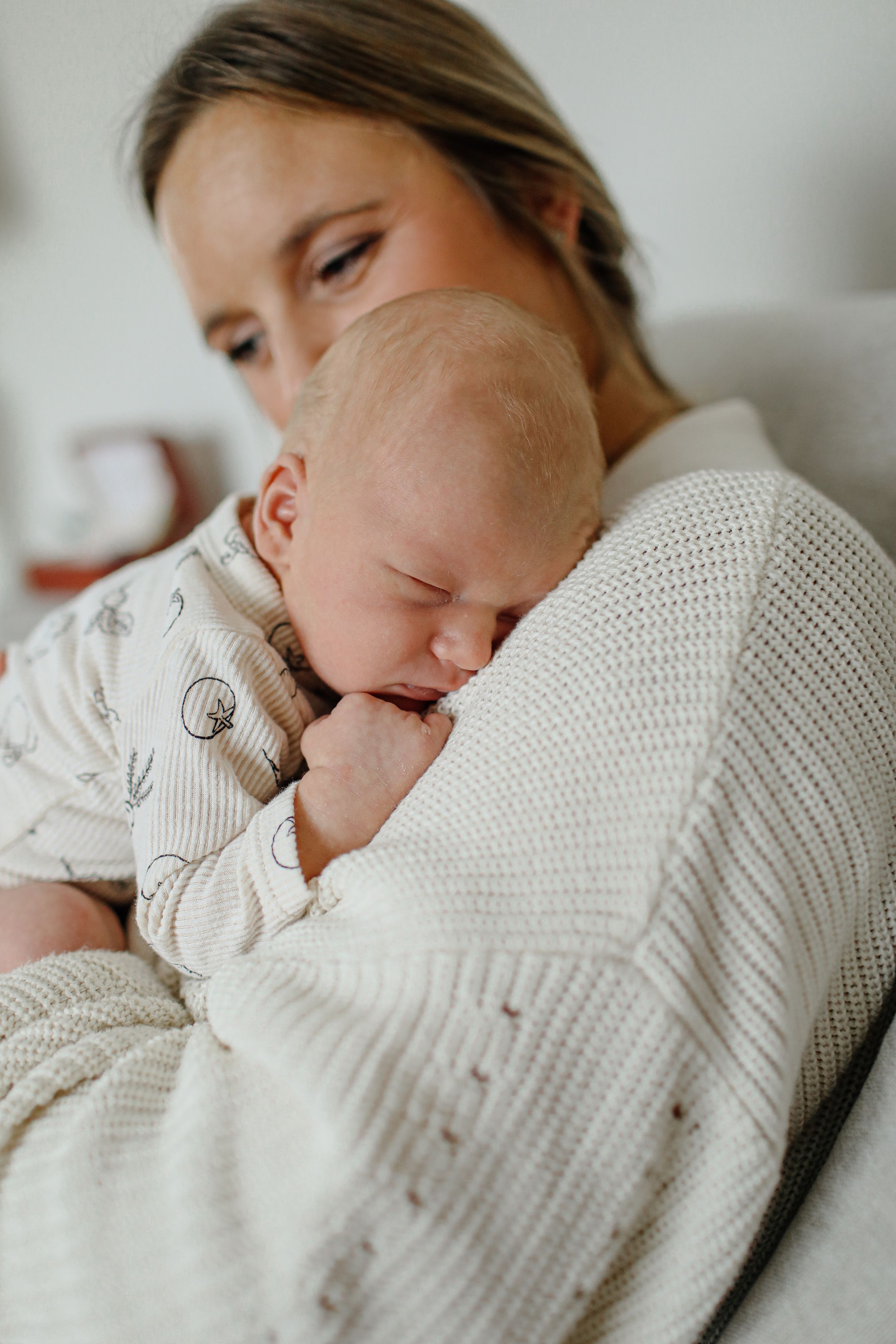 Intimate moment of parent and sleeping baby cuddling in cozy white sweater.