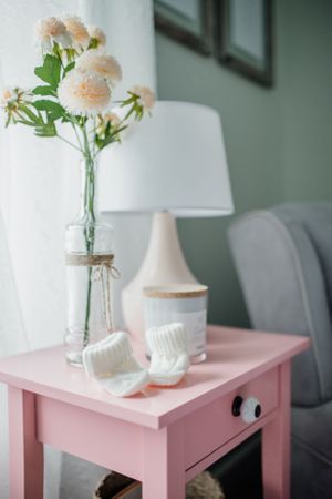 Pink side table with flowers in a mason jar and white lamp creates a cozy bedroom corner.
