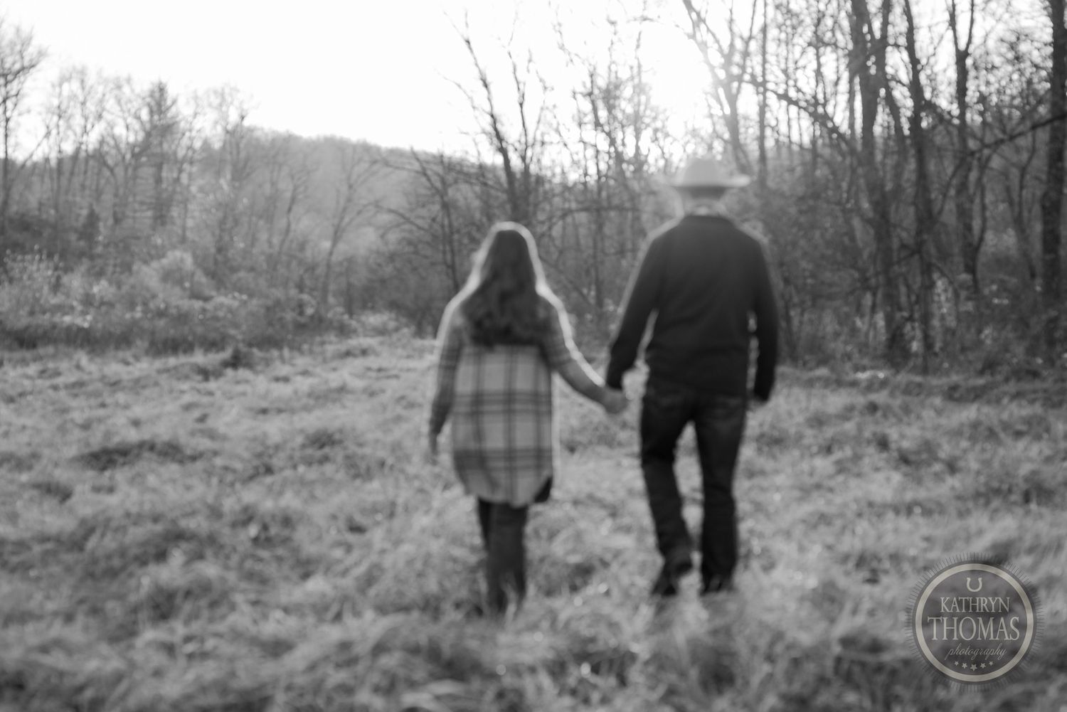 Black and white image of a couple walking hand in hand on a hillside path.