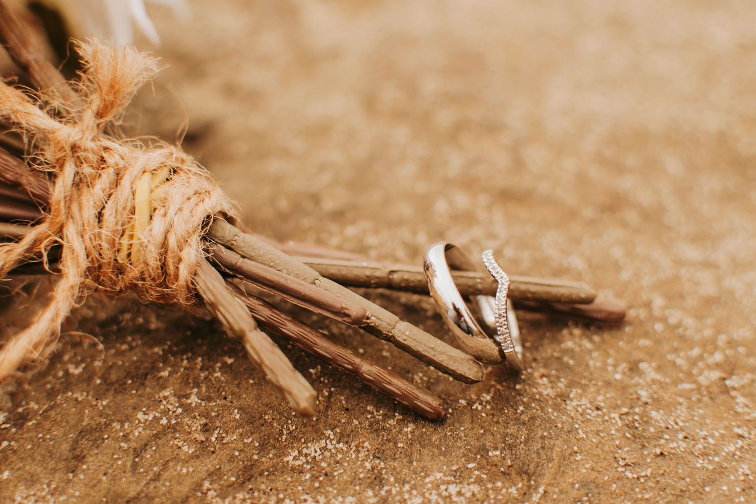 Close-up of wedding rings resting on rustic twine-wrapped sticks.