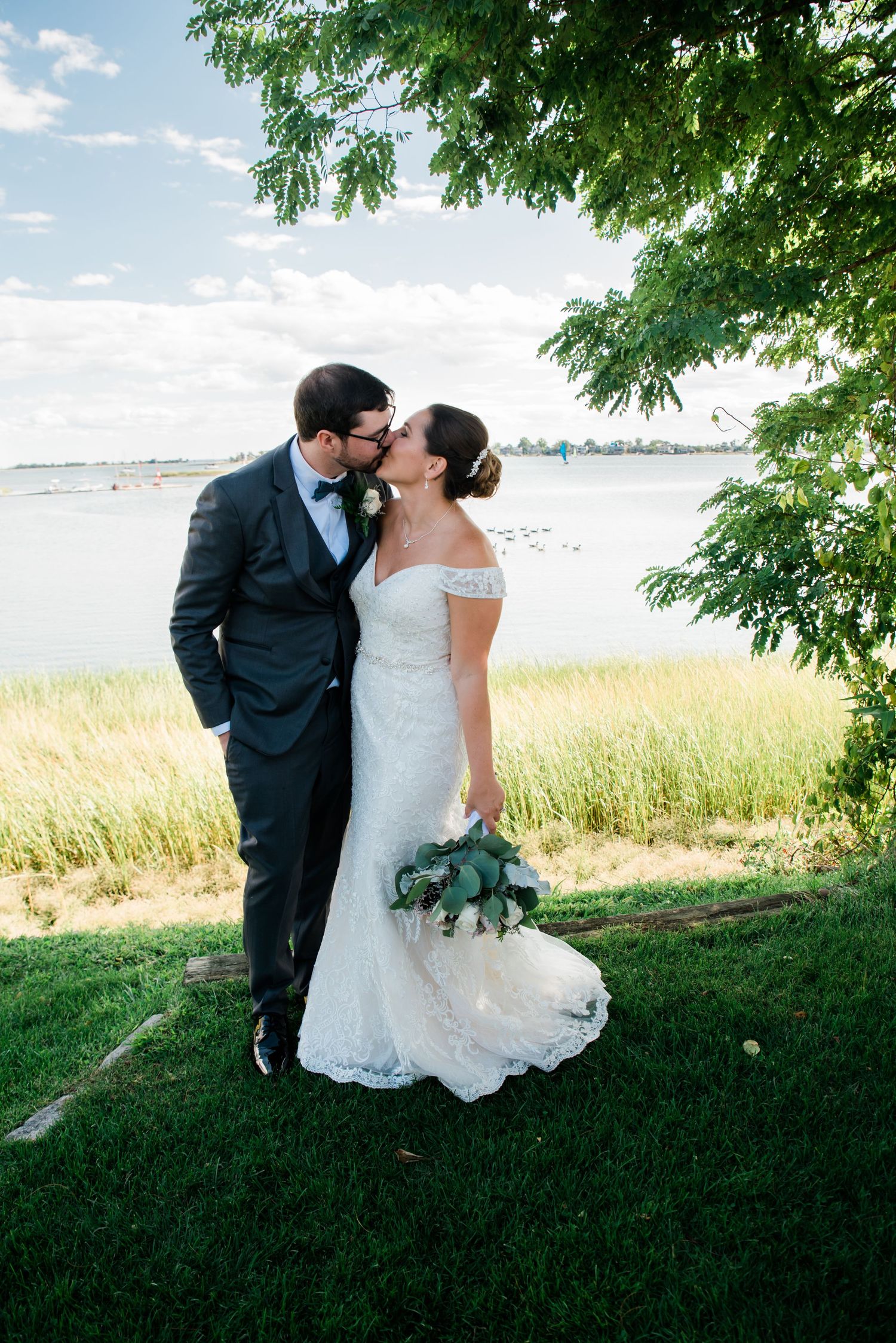 A waterfront wedding portrait with natural scenery and flowing white dress.