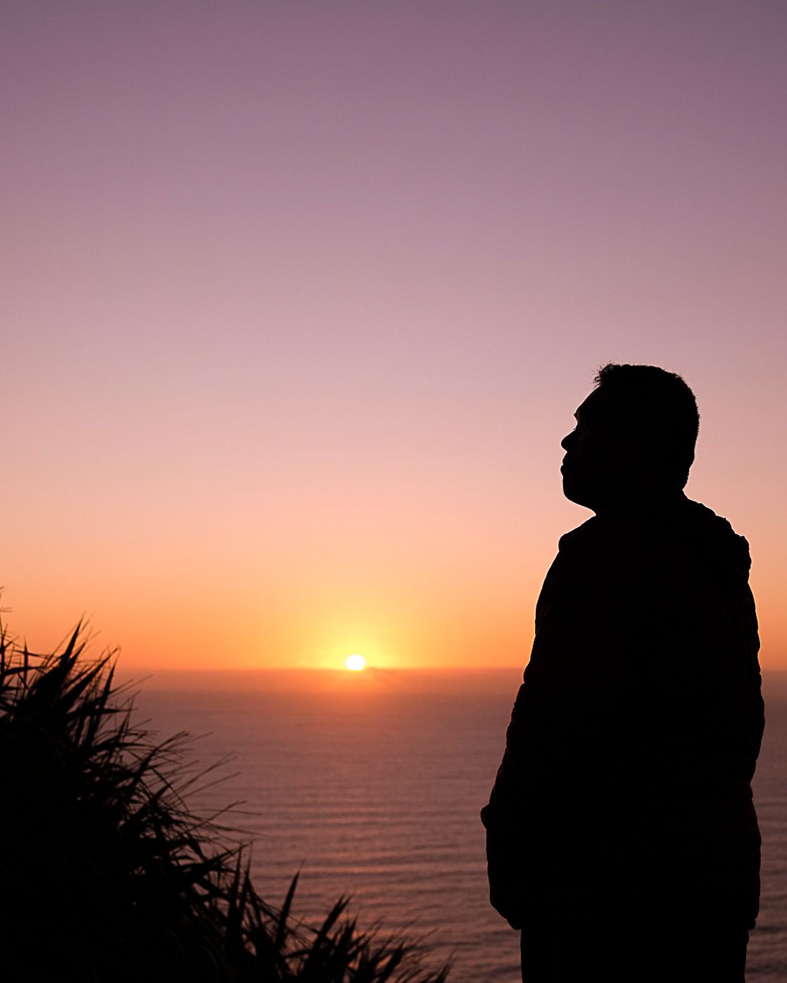Silhouette figure against orange sunset sky over ocean horizon.