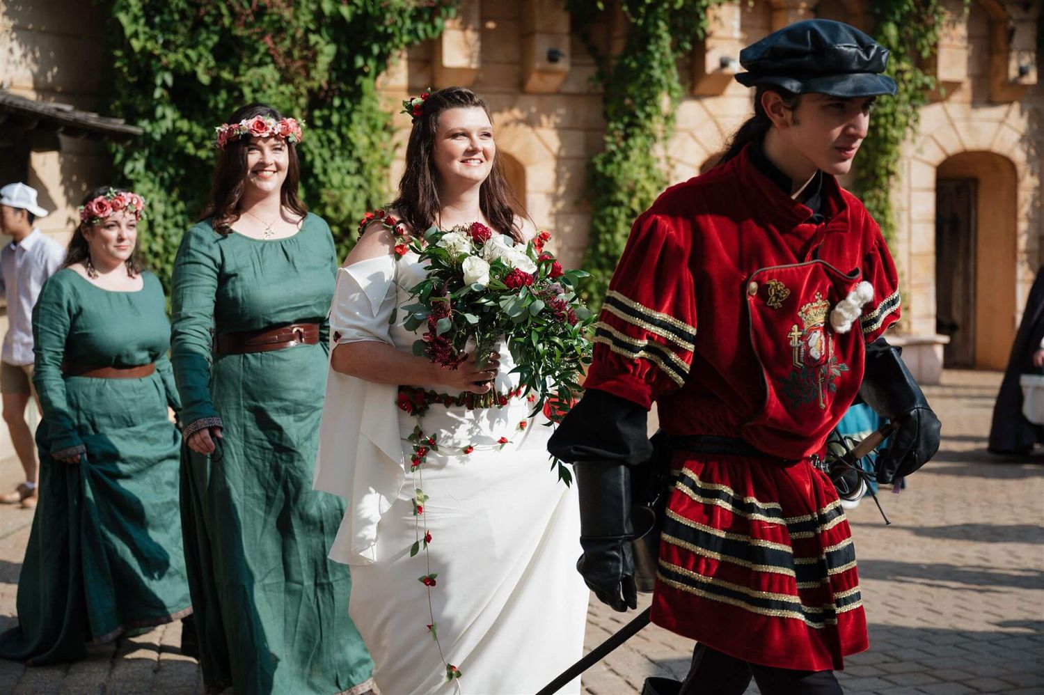 Renaissance festival attendees wearing medieval gowns and costumes walk together outdoors.