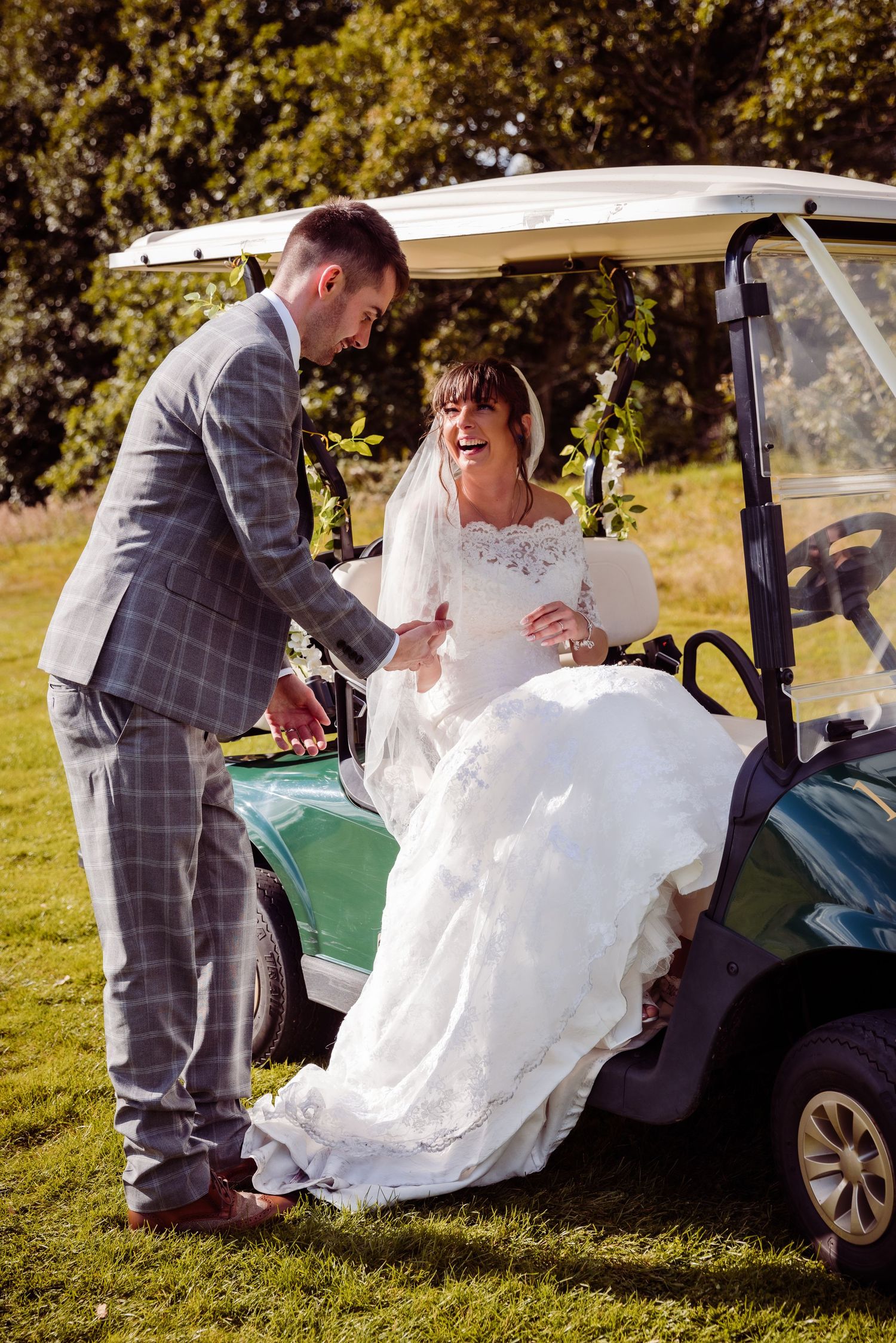 A couple shares a laughing moment next to a golf cart on their wedding day.