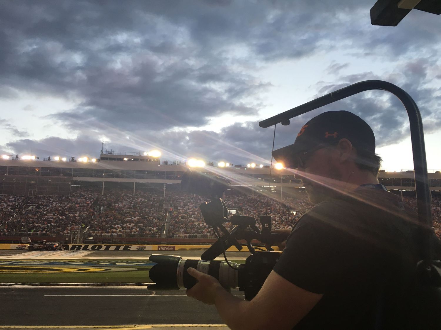 Silhouetted camera operator films at a crowded sports stadium during sunset.