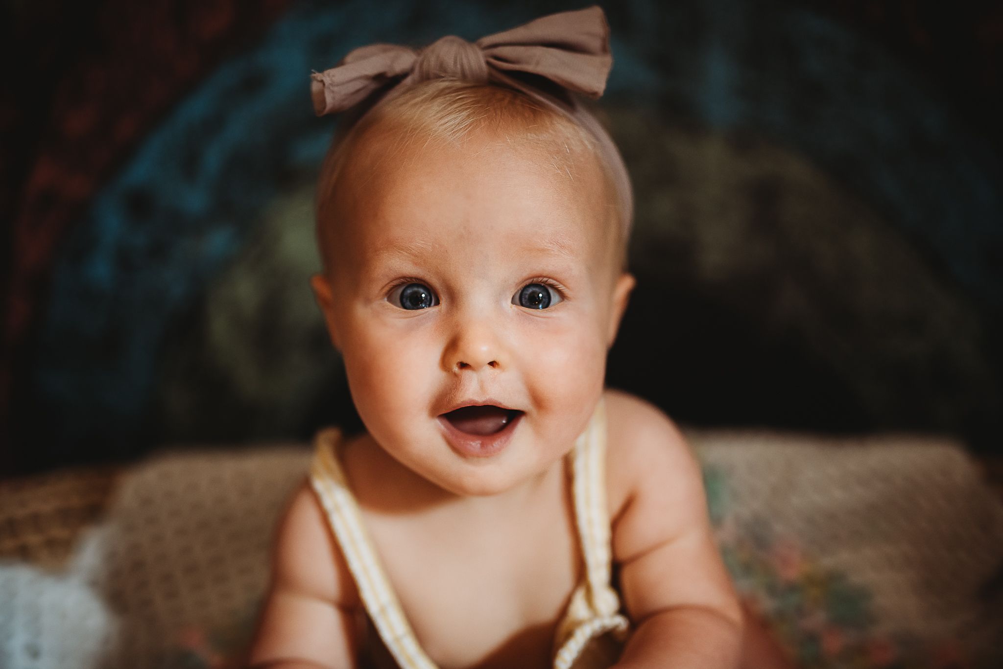 Baby girl posed in basket in front of rainbow with bow on head for family photo shoot