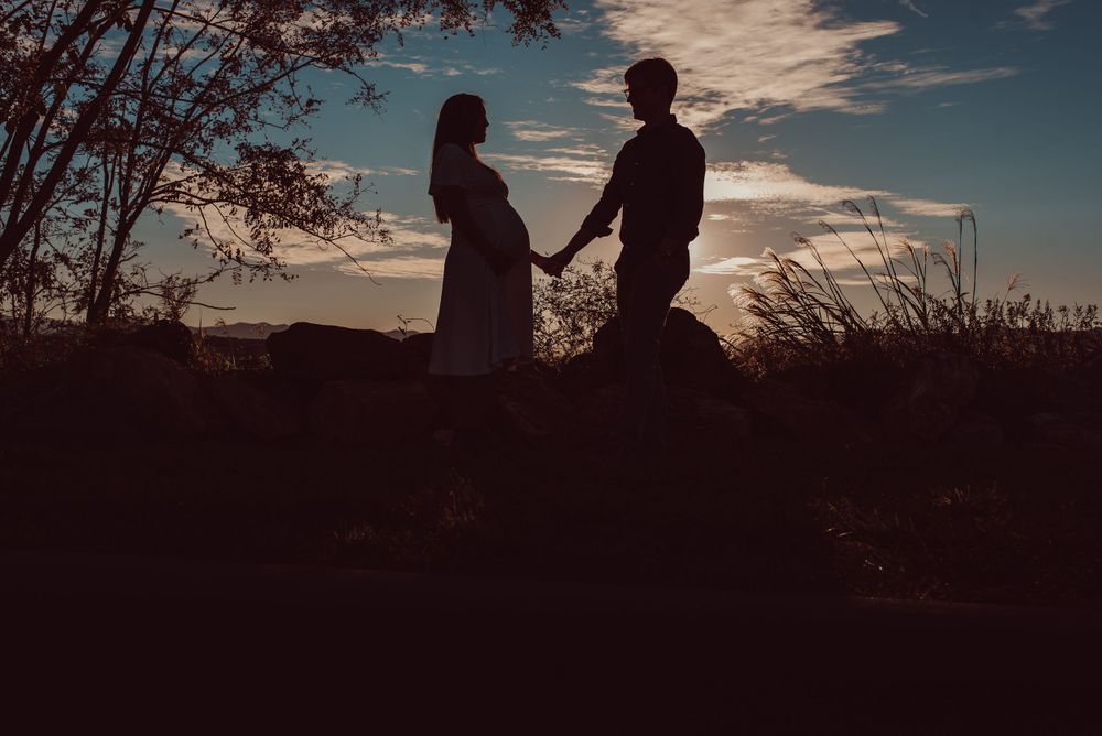 Outline of man and pregnant woman holding hands with sunset behind them during maternity photoshoot.