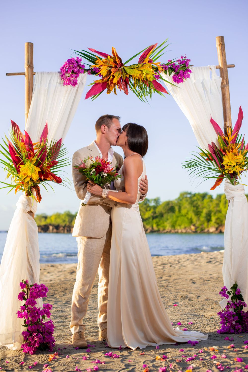Tropical beach wedding ceremony setup with colorful floral arrangements and white fabric draping on the sand.
