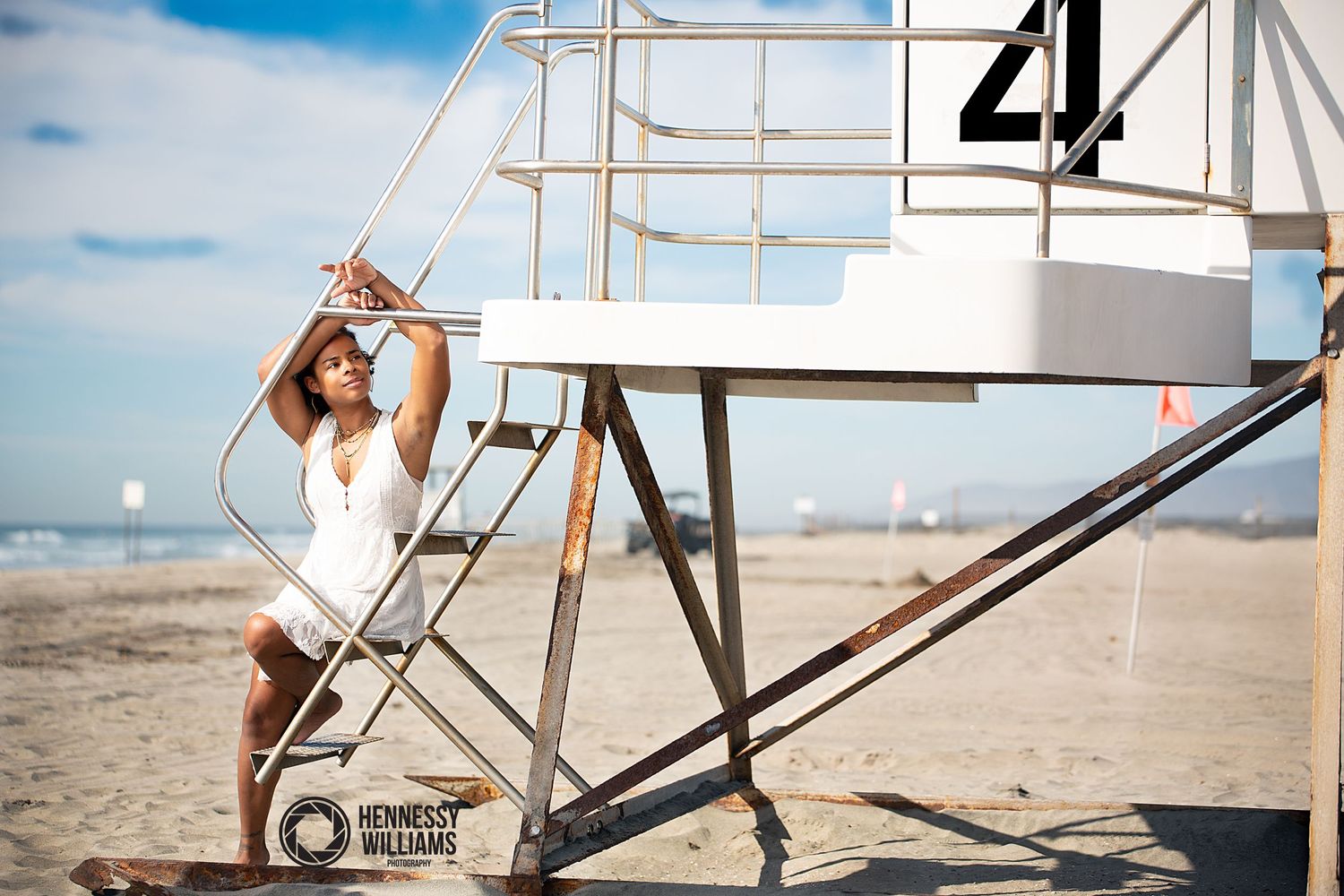 A lifeguard stands alert at their station on a sunny beach with a blue sky in the background.