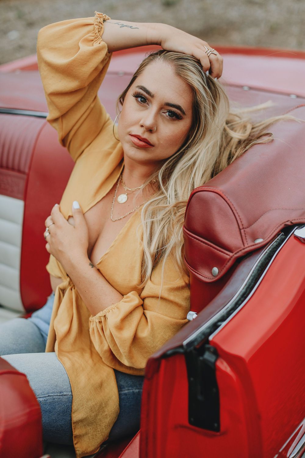 A person in a yellow sweater poses inside a vintage red convertible car with burgundy leather seats.