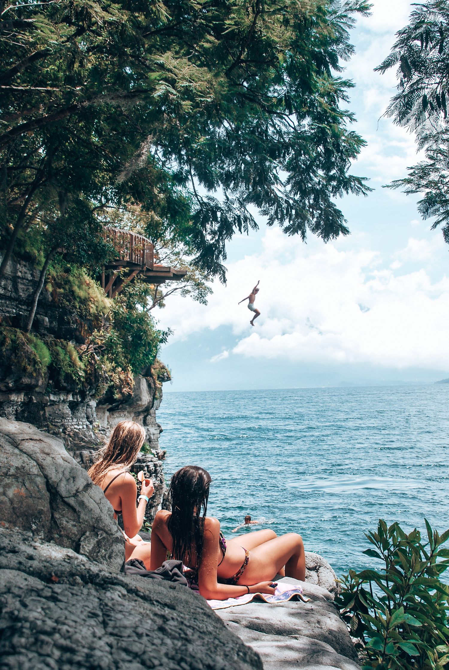 someone cliff jumping in a lake while being watching by girls