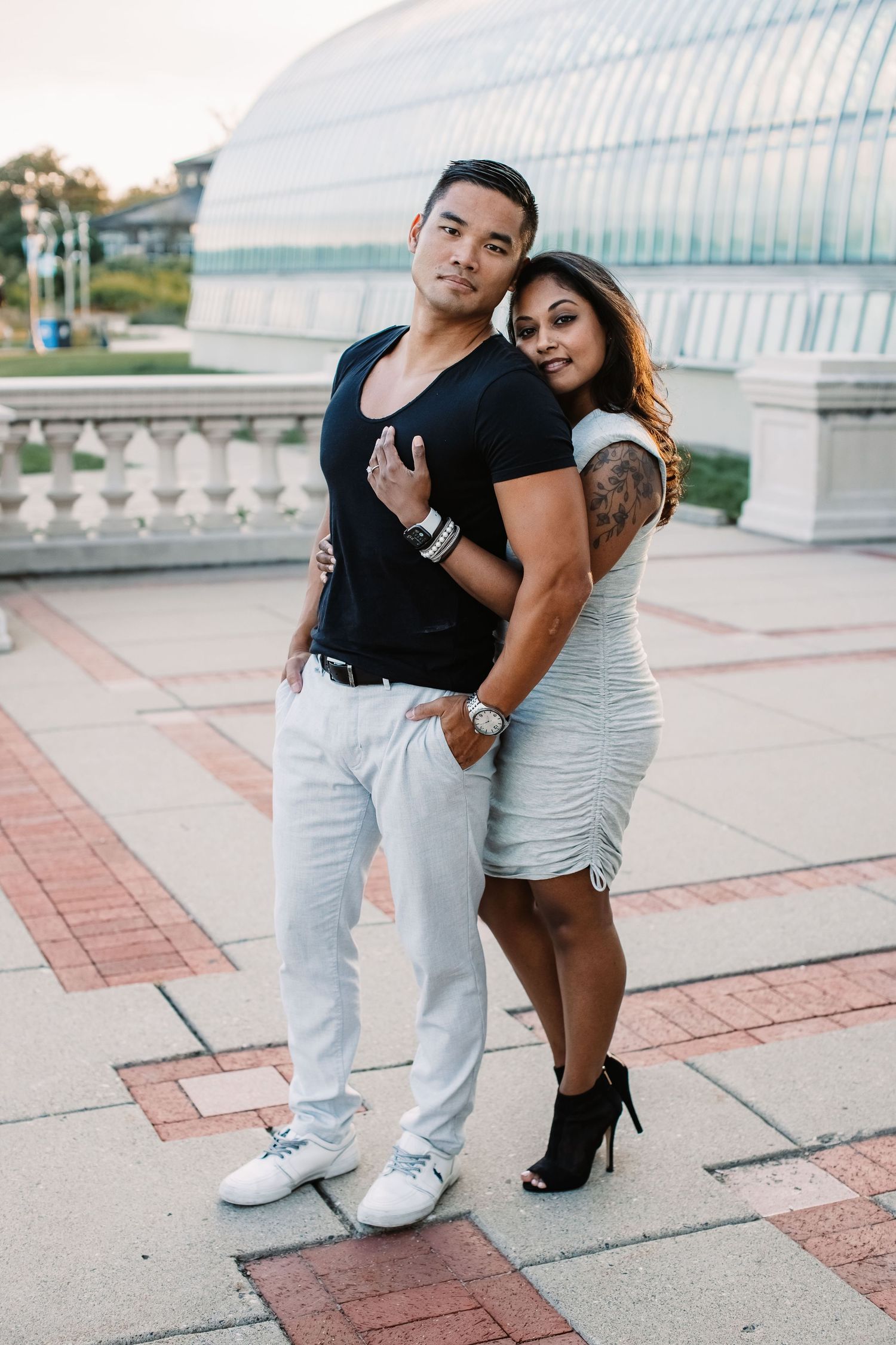 A stylish couple poses together in front of a modern glass building.
