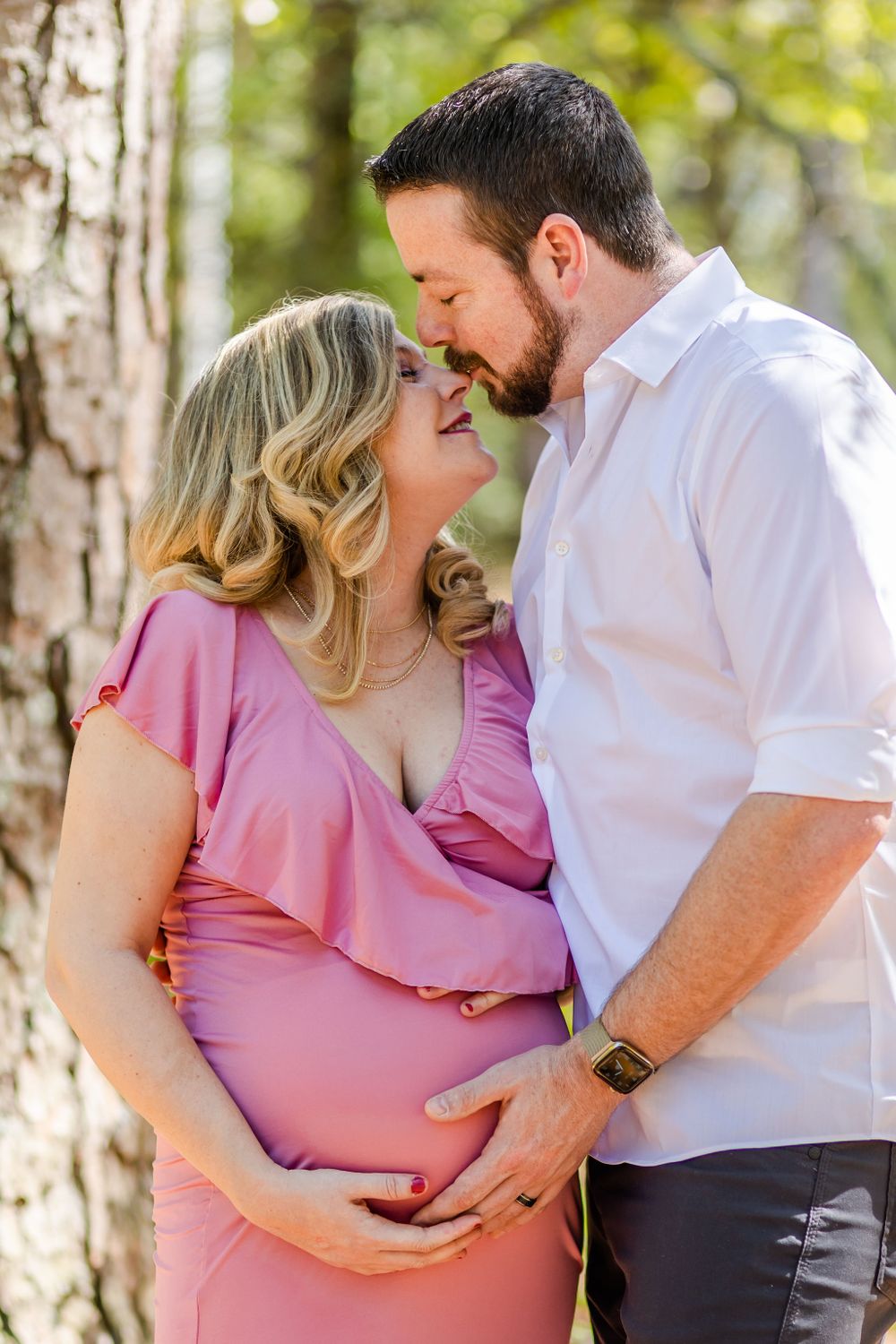 Intimate maternity portrait of couple sharing tender moment against birch trees in forest setting.