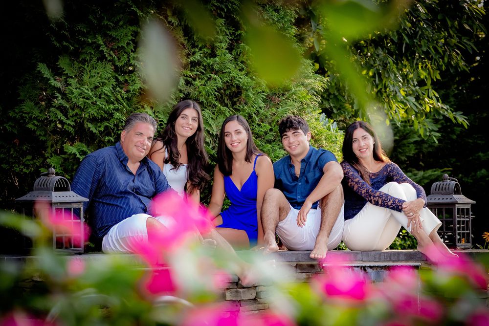 Family group seated in garden with vibrant pink flowers in foreground.