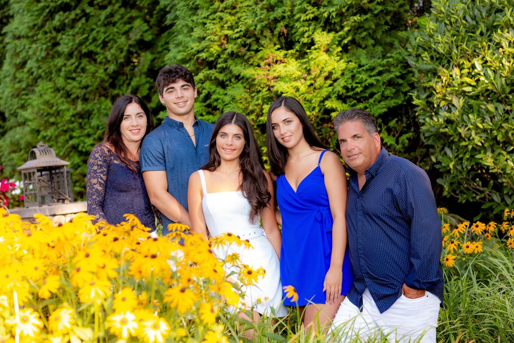 Family portrait in garden with bright yellow flowers and lush greenery.
