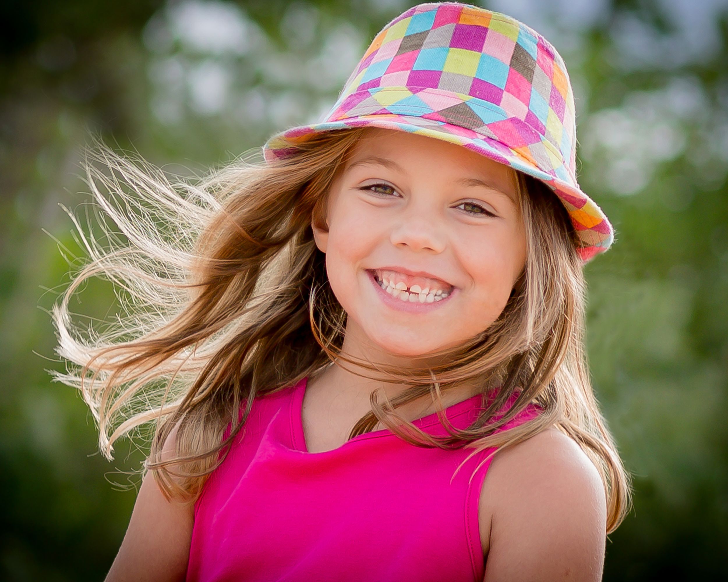 Candid outdoor shot featuring colorful checkered bucket hat and pink top with wind-blown hair.