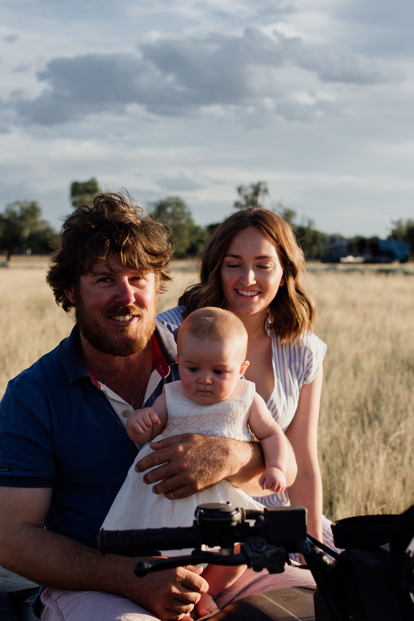 Father and Mother with 6 month old sitting sitting on quad bike in the paddock on their farm during golden hour
