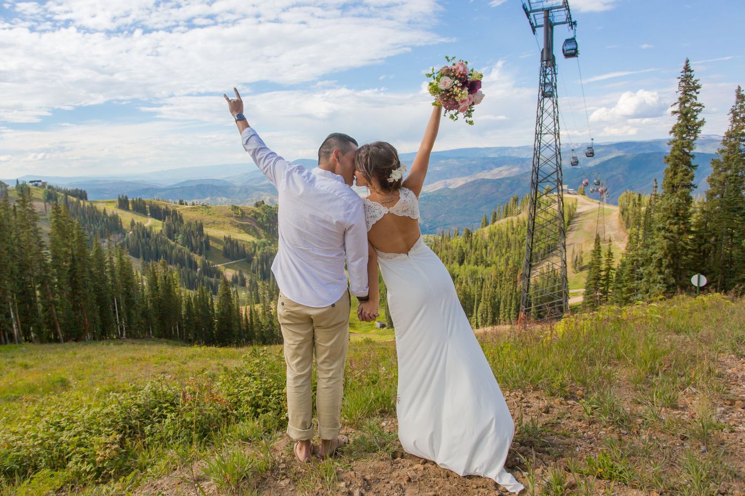 A couple celebrates on a mountainside with scenic valley views and ski lifts in the background.